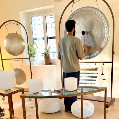 A practitioners seated with eyes closed, bathed in the vibrations of a large gong played by a facilitator.